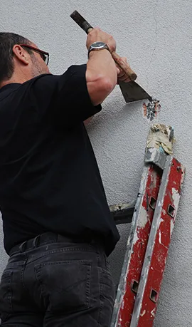 Sachverständiger öffnet eine Putzfläche mit dem Meißel